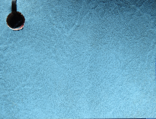 Tropical Blue Blue textured surface with a black circular object in the top left corner.